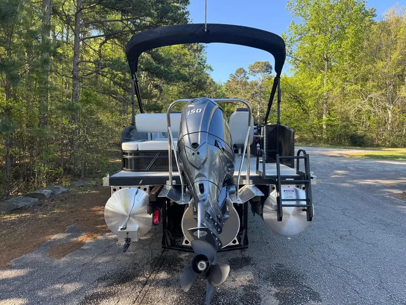 Slide: The Image of 2025 Bennington 22SSB pontoon boat with outboard motor, parked on a forested road. - 20
