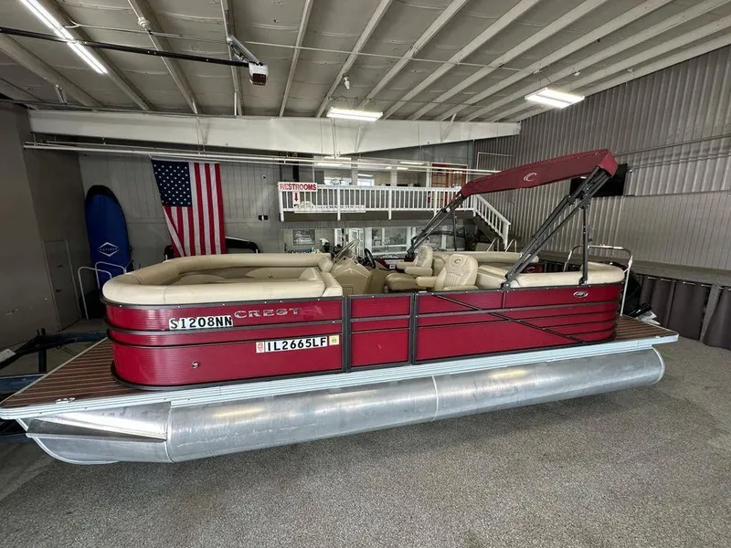 Slide: The Image of 2018 Crest Classic 230 SLC pontoon boat in showroom, red exterior, beige interior, American flag backdrop. - 1