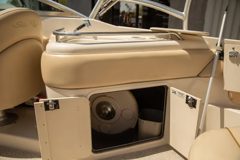 Slide: The Image of 2002 Sea Ray 240 Sundeck interior storage compartment with open door, showcasing beige seating. - 11