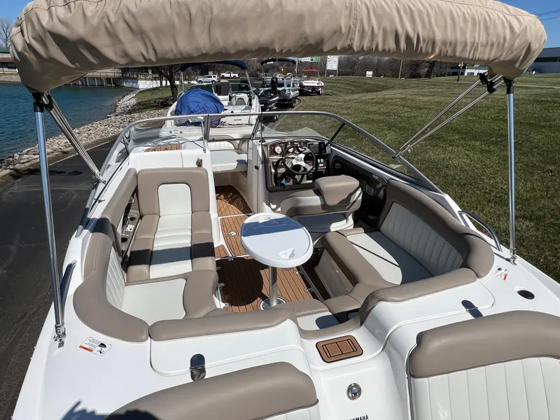 Slide: The Image of 2008 Yamaha Boats 232 Limited with beige seating and canopy, docked near a grassy shoreline. - 12