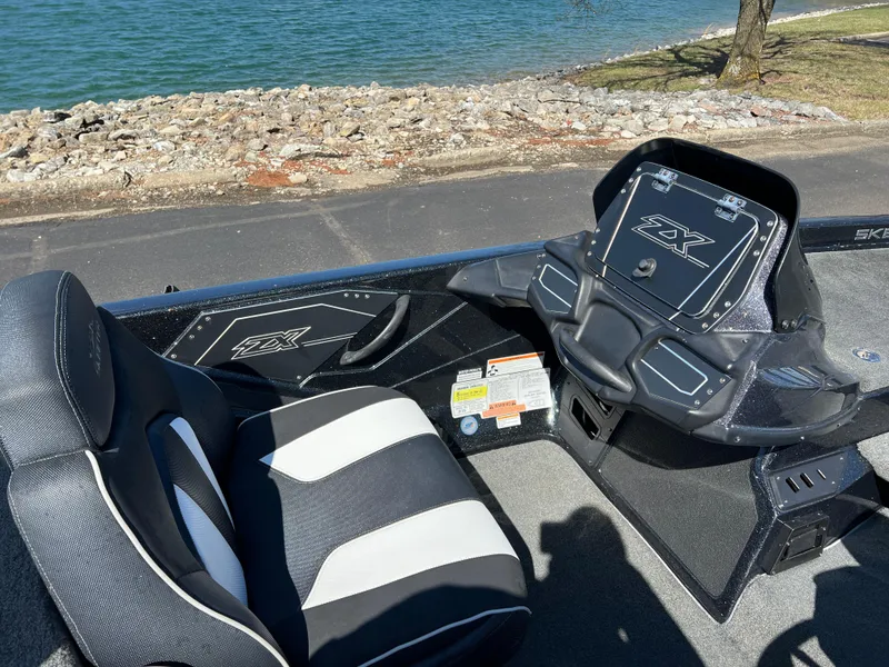 Slide: The Image of 2018 Skeeter ZX 225 boat interior with black and white seating by a lakeside. - 17