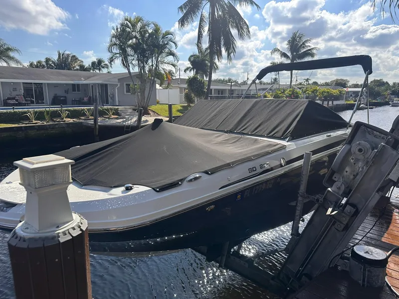 Slide: The Image of 2022 Hurricane SunDeck 235 OB boat docked, covered, with palm trees and waterfront homes in the background. - 25