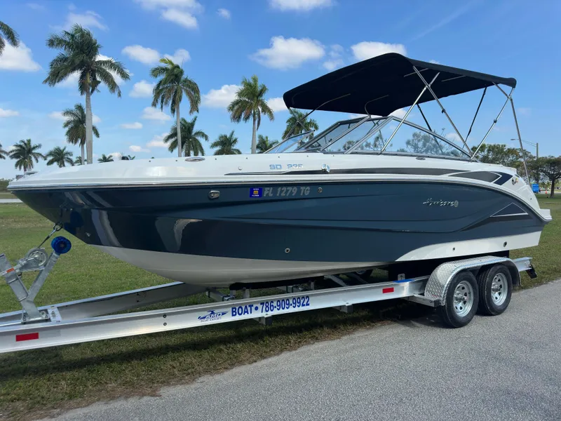 Slide: The Image of 2022 Hurricane SunDeck 235 OB boat on trailer, parked near palm trees under blue sky. - 7