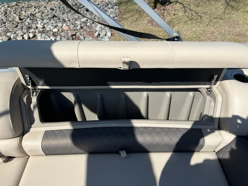 Slide: The Image of 2023 Sun Tracker Party Barge 20 DLX storage compartment with open lid, beige seating, and shadow. - 23