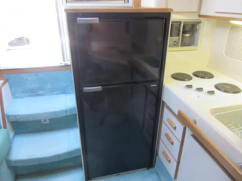 Slide: The Image of 1995 Sea Ray 400 Express Cruiser kitchen with black fridge, stove, and white cabinetry. - 30
