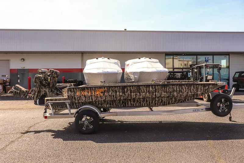 Slide: The Image of 2025 Excel 1754 F4 Shallow Water boat on trailer, camo design, parked outside a building. - 4