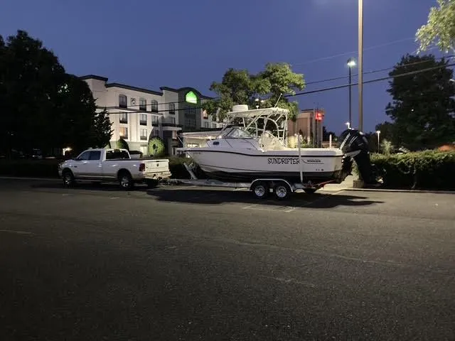 Slide: The Image of 2008 Boston Whaler 235 Conquest boat on trailer, parked beside a white truck at dusk. - 4