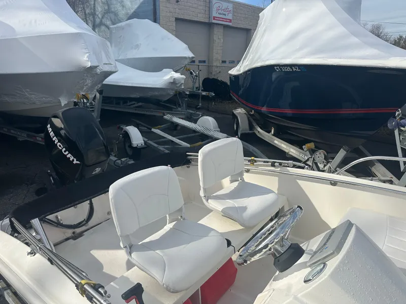 Slide: The Image of 2013 Boston Whaler 150 Super Sport boat with Mercury engine, parked among covered boats. - 16