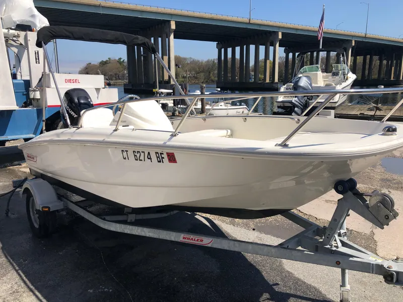 Slide: The Image of 2013 Boston Whaler 150 Super Sport boat on trailer near a bridge. - 20