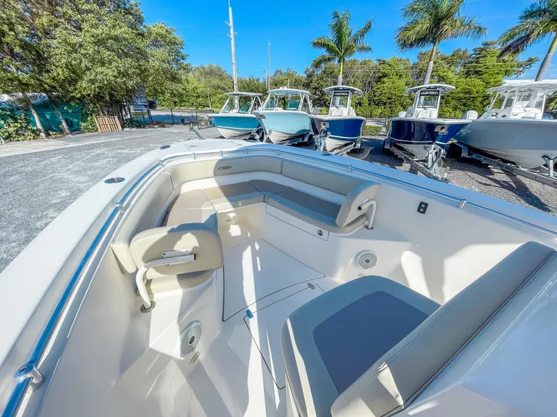 Slide: The Image of 2016 Cobia 277 CC boat interior with seating, surrounded by other boats and palm trees. - 16