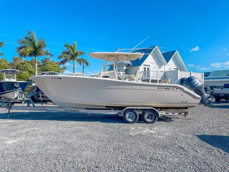 Slide: The Image of 2016 Cobia 277 CC boat on trailer, parked outdoors with palm trees and buildings in the background. - 5