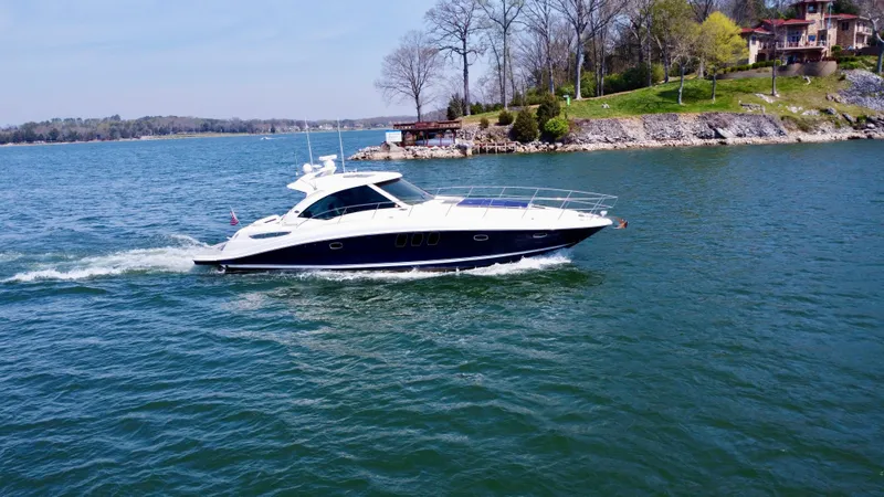 Slide: The Image of 2006 Sea Ray 48 Sundancer yacht cruising on a scenic lake near a wooded shoreline. - 13