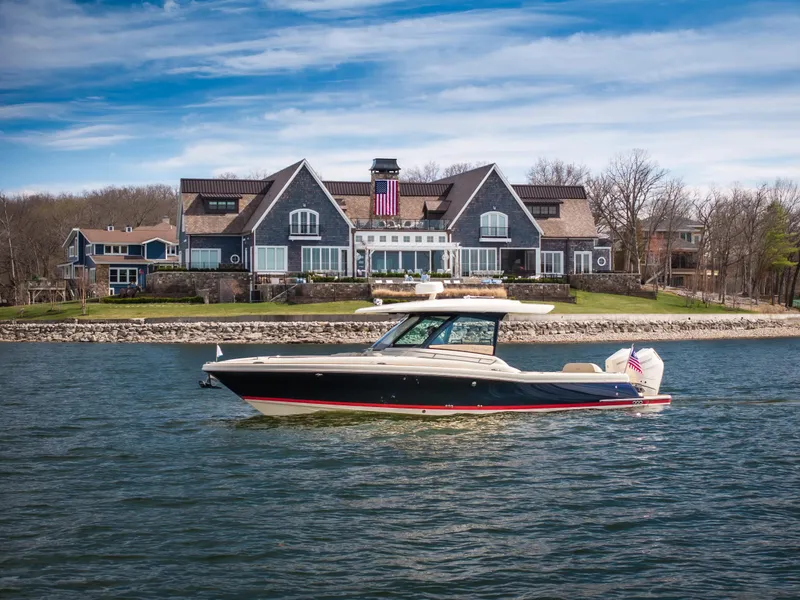 The Image of 2024 Chris-Craft Calypso 35 CP boat cruising near a large waterfront house. - 1