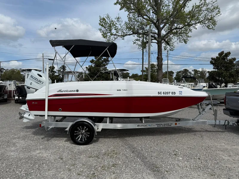 Slide: The Image of 2023 Hurricane SunDeck Sport 188 OB boat on trailer, red and white design, parked outdoors. - 0
