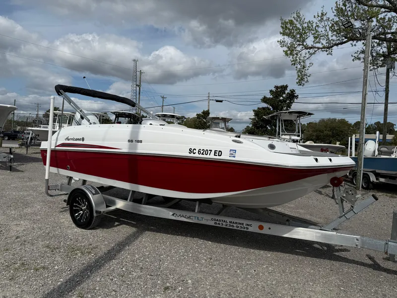 Slide: The Image of 2023 Hurricane SunDeck Sport 188 OB boat on trailer, red and white design, parked outdoors. - 14