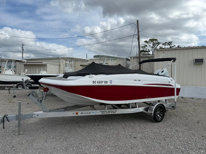 Slide: The Image of 2023 Hurricane SunDeck Sport 188 OB boat on trailer, red and white design, outdoor storage. - 18