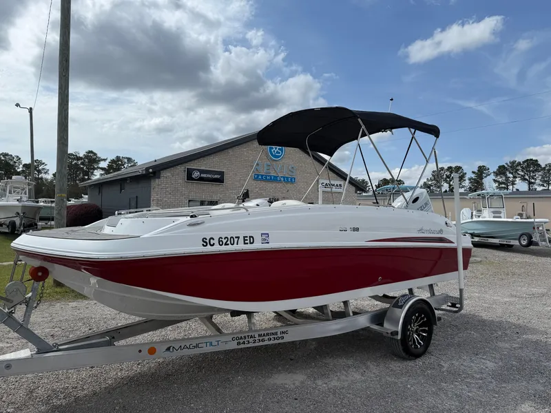 Slide: The Image of 2023 Hurricane SunDeck Sport 188 OB boat on trailer, red and white design, parked outdoors. - 2