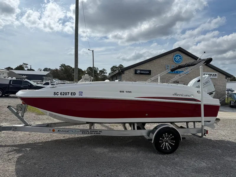 Slide: The Image of 2023 Hurricane SunDeck Sport 188 OB boat on trailer, red and white design, parked outdoors. - 7