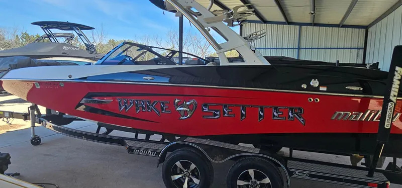 Slide: The Image of 2013 Malibu Wakesetter 23 MXZ boat in red and black, parked in a covered area. - 9