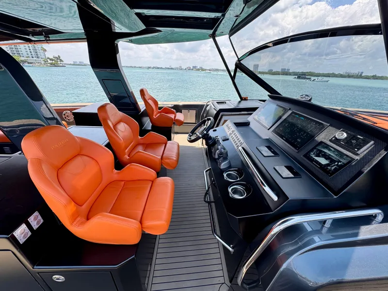 Slide: The Image of 2023 Pardo Yachts 50 cockpit with orange seats and modern dashboard, overlooking the ocean. - 16