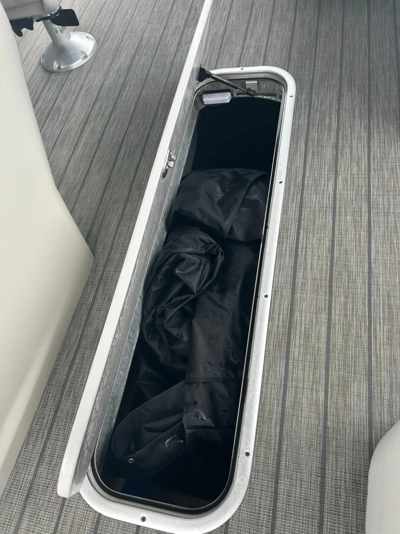 Slide: The Image of 2021 Avalon Catalina 24' storage compartment with black cover on gray flooring. - 24
