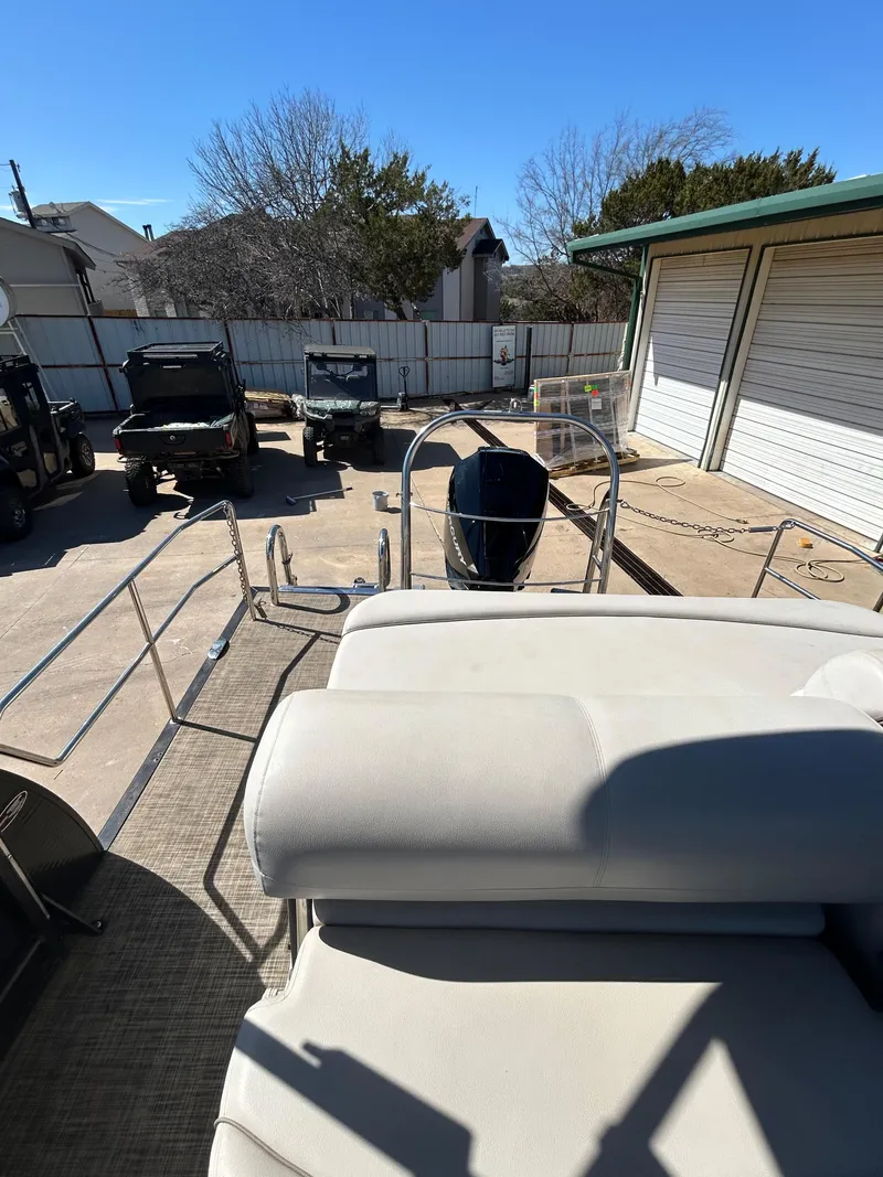 Slide: The Image of 2019 Harris Sunliner 240 pontoon boat in a driveway, surrounded by vehicles and garages. - 11