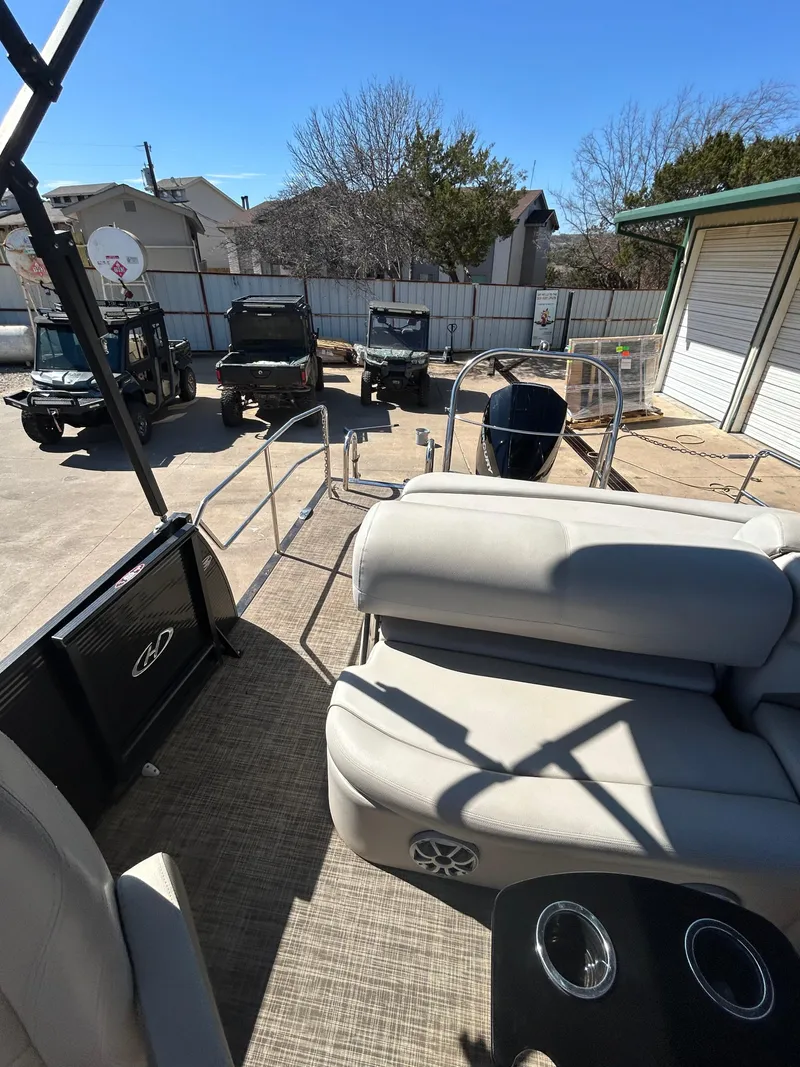 Slide: The Image of 2019 Harris Sunliner 240 pontoon boat interior with seating and cup holders, parked near utility vehicles. - 12