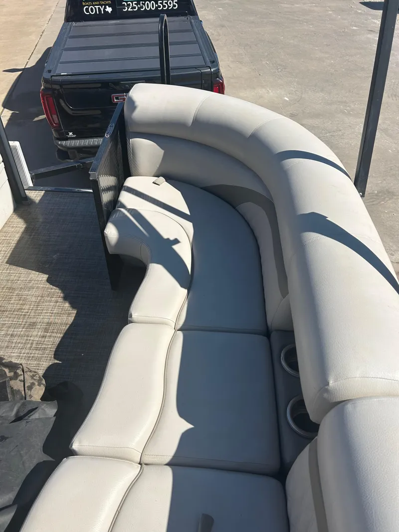 Slide: The Image of 2019 Harris Sunliner 240 boat with spacious seating and cup holders, parked near a black truck. - 31