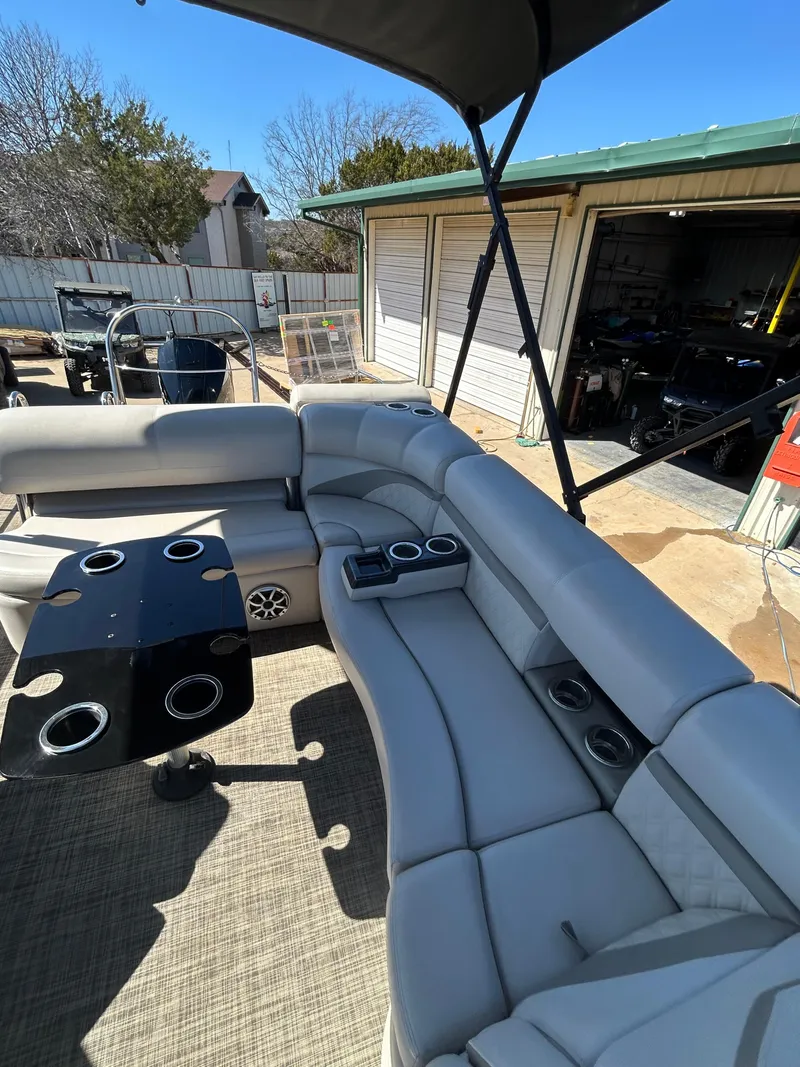 Slide: The Image of 2019 Harris Sunliner 240 pontoon boat with spacious seating and cup holders, parked near a garage. - 8
