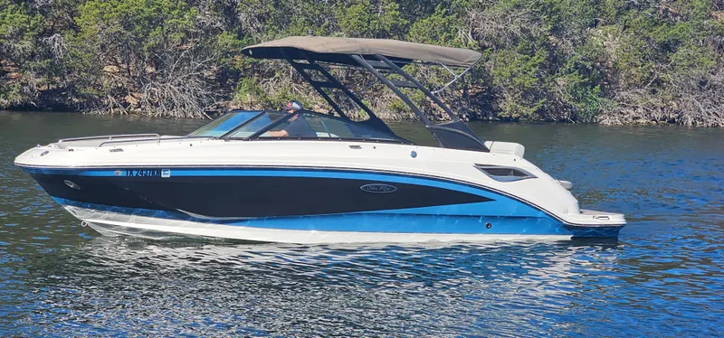 Slide: The Image of 2022 Sea Ray SDX 250 boat cruising on a calm lake with lush greenery. - 17