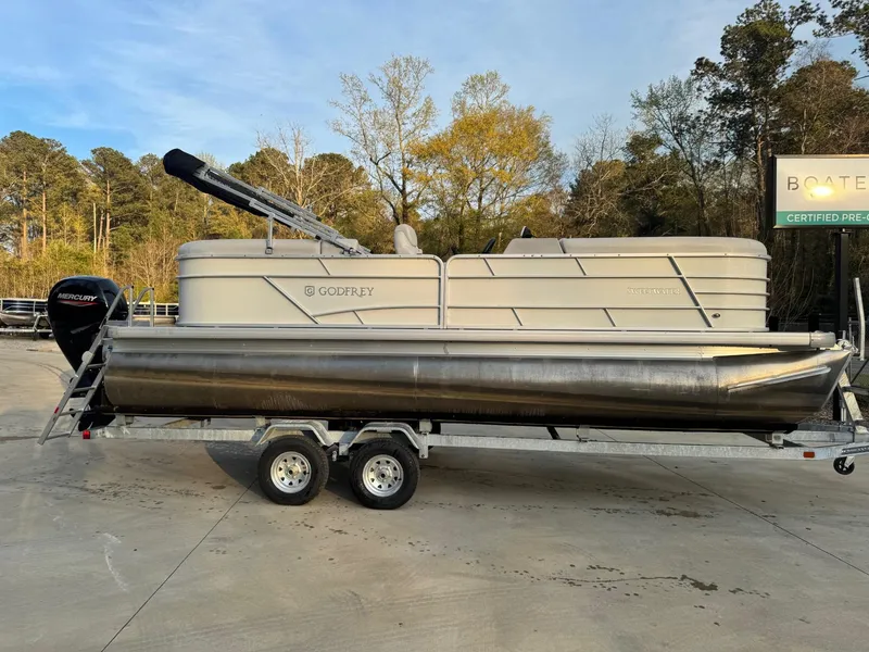 Slide: The Image of 2022 Godfrey 2286 pontoon boat on trailer, parked outdoors with trees in background. - 2