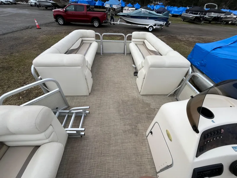 Slide: The Image of Bennington LX 2280 pontoon boat interior with beige seating, parked near covered boats. - 7