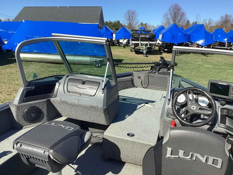 Slide: The Image of 2016 Lund 1775 Impact boat interior with steering wheel, seats, and dashboard, parked outdoors. - 6