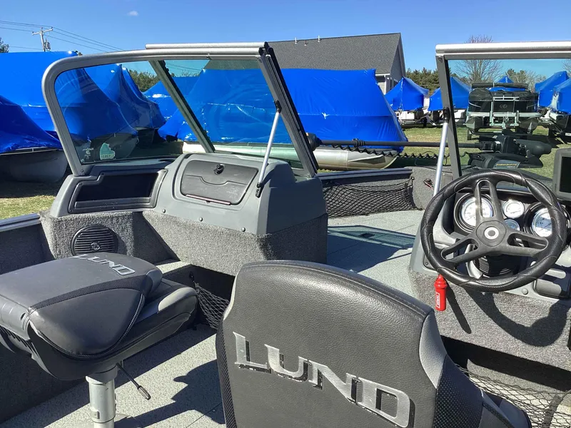 Slide: The Image of 2016 Lund 1775 Impact boat interior with steering wheel and seating, parked outdoors. - 9