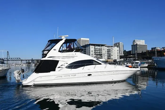 The Image of 2006 Sea Ray 44 Sedan Bridge yacht docked in urban marina, clear blue sky. - 0
