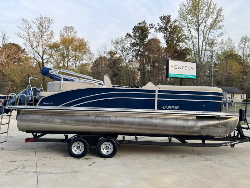 Slide: The Image of 2023 Harris 230 Cruiser pontoon boat on a trailer, parked outdoors. - 2