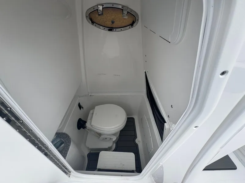 Slide: The Image of 2025 NauticStar 292 Legacy boat interior bathroom with compact toilet and porthole. - 22