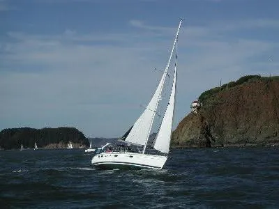 Slide: The Image of Sailboat Hunter 380 (1999) navigating near rocky coastline under clear skies. - 2