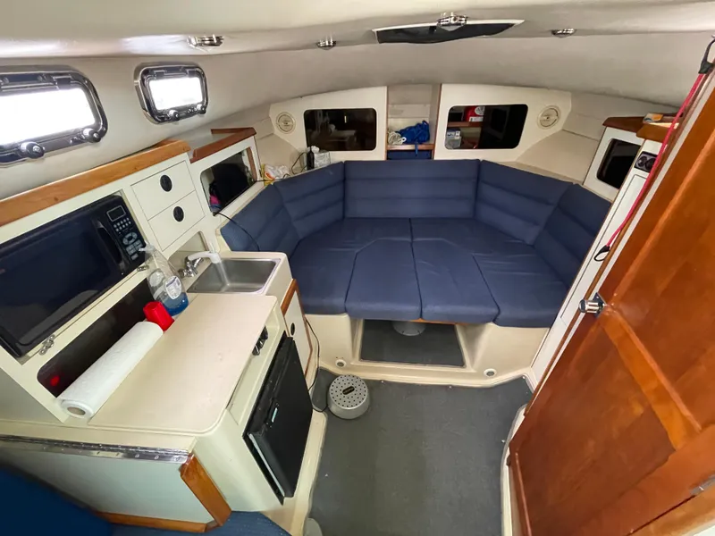 Slide: The Image of 2004 Albin 30 Family Cruiser interior with blue seating and compact kitchen area. - 29