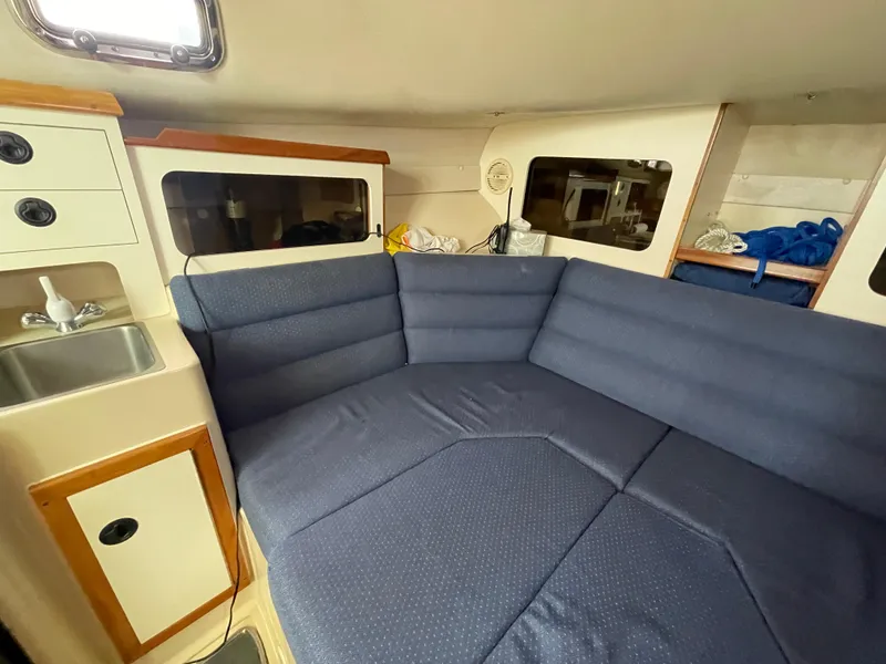 Slide: The Image of 2004 Albin 30 Family Cruiser interior with blue cushioned seating and compact kitchenette. - 31