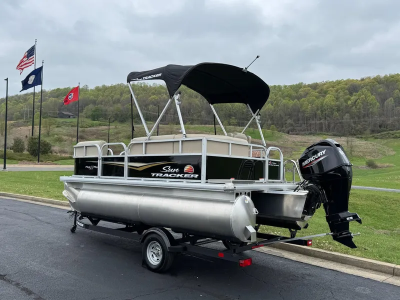 Slide: The Image of 2025 Sun Tracker Party Barge 16 DLX pontoon boat on trailer, flags in background. - 2