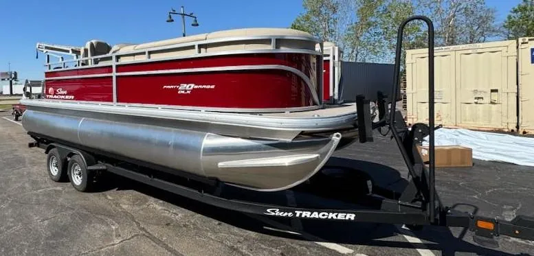 Slide: The Image of 2025 Sun Tracker Party Barge 20 DLX pontoon boat on trailer, parked outdoors. - 2