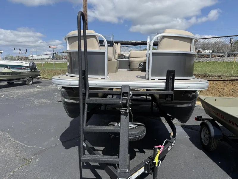 Slide: The Image of 2025 Sun Tracker Party Barge 16 DLX pontoon boat on trailer, parked outdoors. - 2