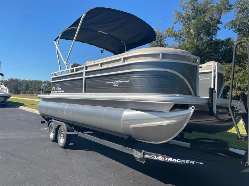 Slide: The Image of 2025 Sun Tracker Party Barge 20 DLX pontoon boat on trailer, parked outdoors. - 2