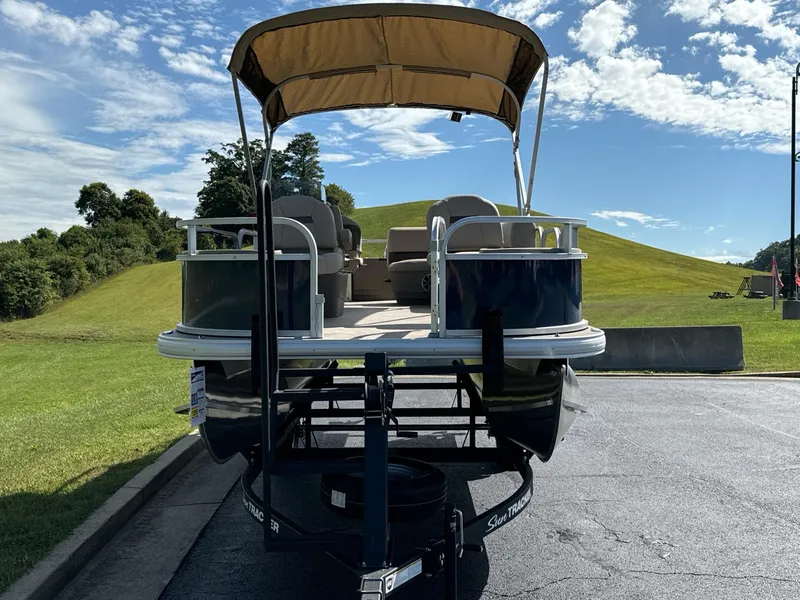 Slide: The Image of 2025 Sun Tracker Bass Buggy 18 DLX pontoon boat on trailer, parked outdoors. - 2
