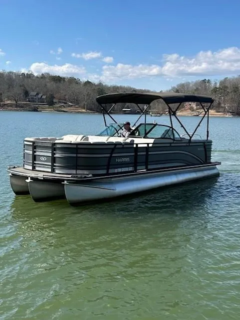 Slide: The Image of 2017 Harris Solstice 250 DC pontoon boat cruising on a lake under a clear blue sky. - 0