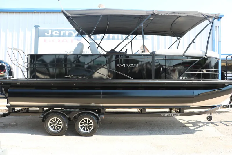 Slide: The Image of 2025 Sylvan Mirage X3 Party Fish pontoon boat on trailer, black exterior, under canopy. - 16