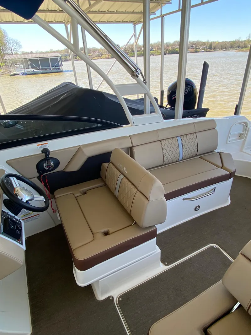 Slide: The Image of 2016 Sea Ray 270 Sundeck interior with beige seating and steering wheel, docked by a lake. - 11