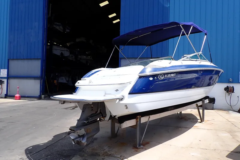 Slide: The Image of 2002 Cobalt 240 boat with blue canopy, parked outside a blue warehouse. - 1