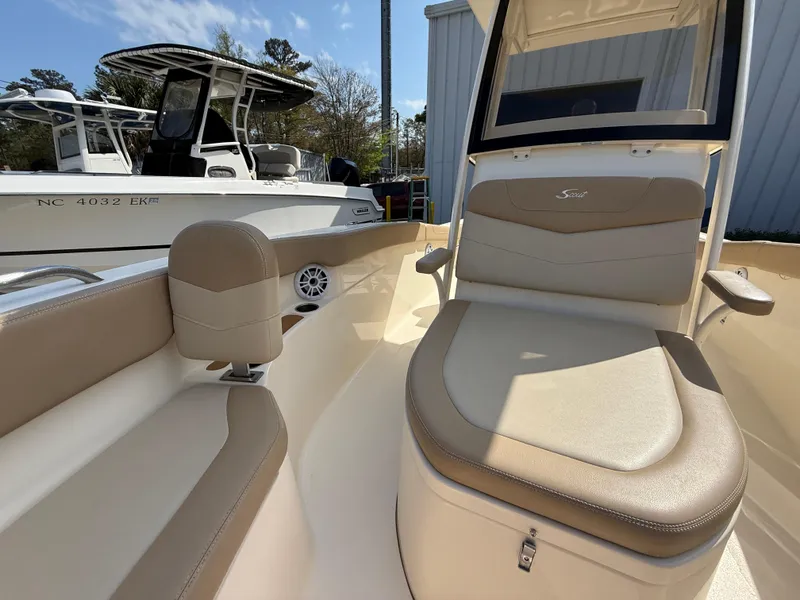 Slide: The Image of 2023 Scout 215 XSF boat interior with beige seating and console, parked outdoors. - 42